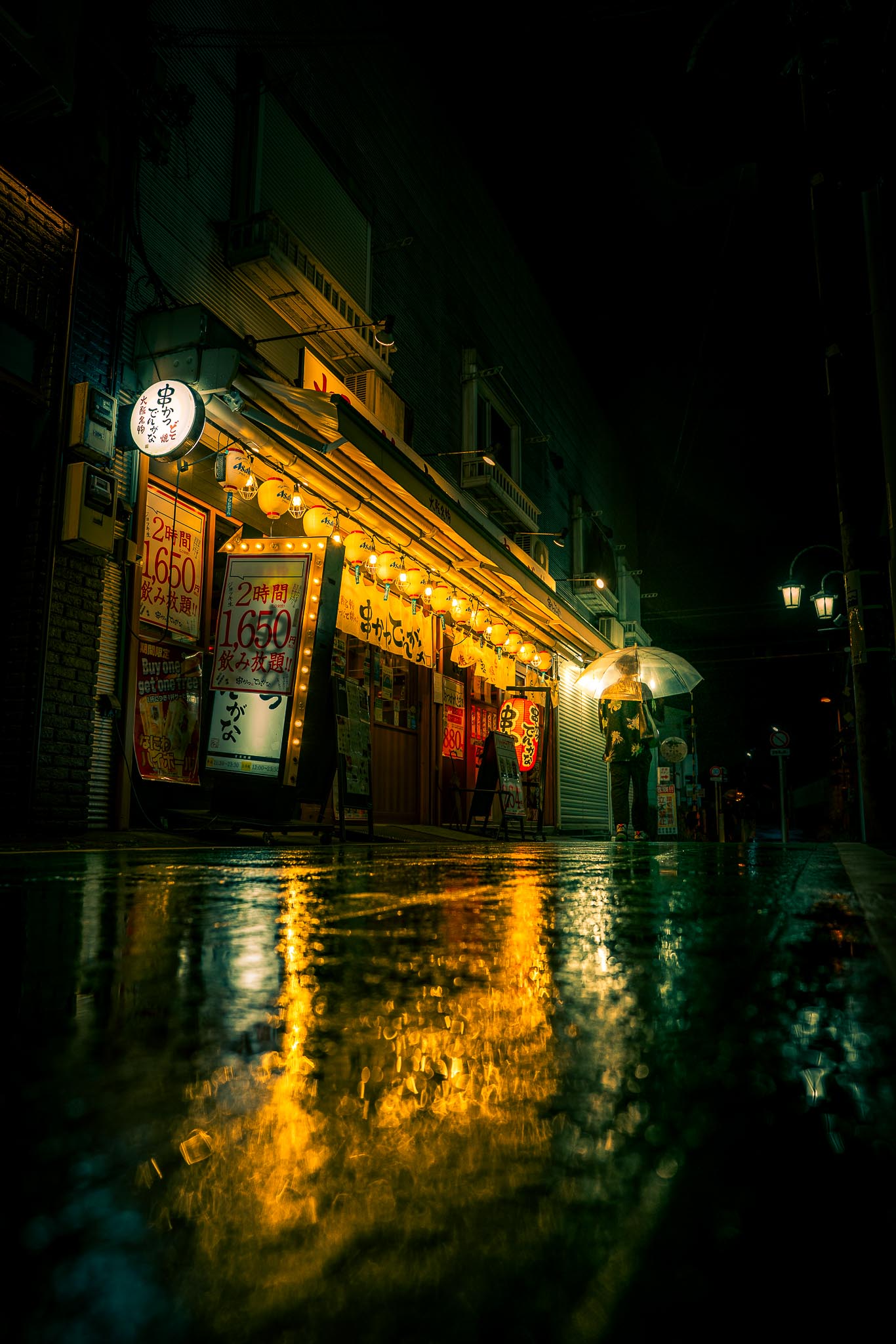 Bubaigawara izakaya at night — umbrella figure and lantern reflections in rain Tokyo