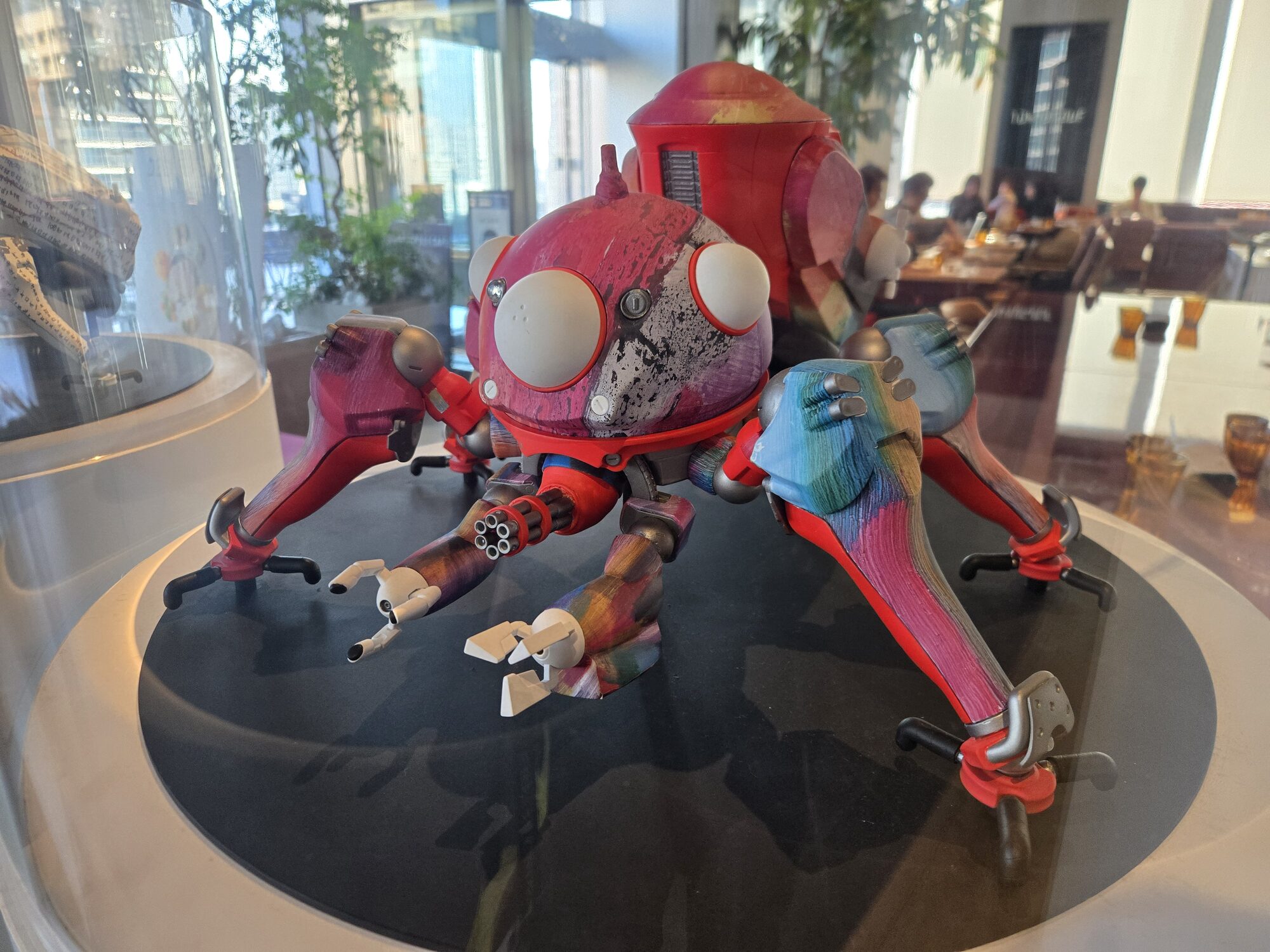 Red and rainbow weathered Tachikoma model in glass display case at Ghost in the Shell Exhibition café, Toranomon Hills