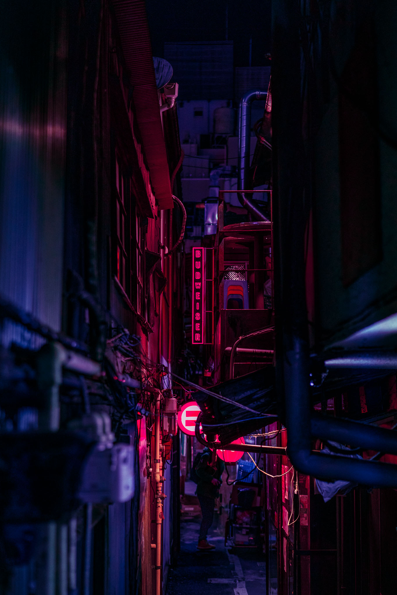 Narrow alley in Harmonica Yokocho, Kichijoji, lit pink by a Budweiser sign with a figure walking toward it