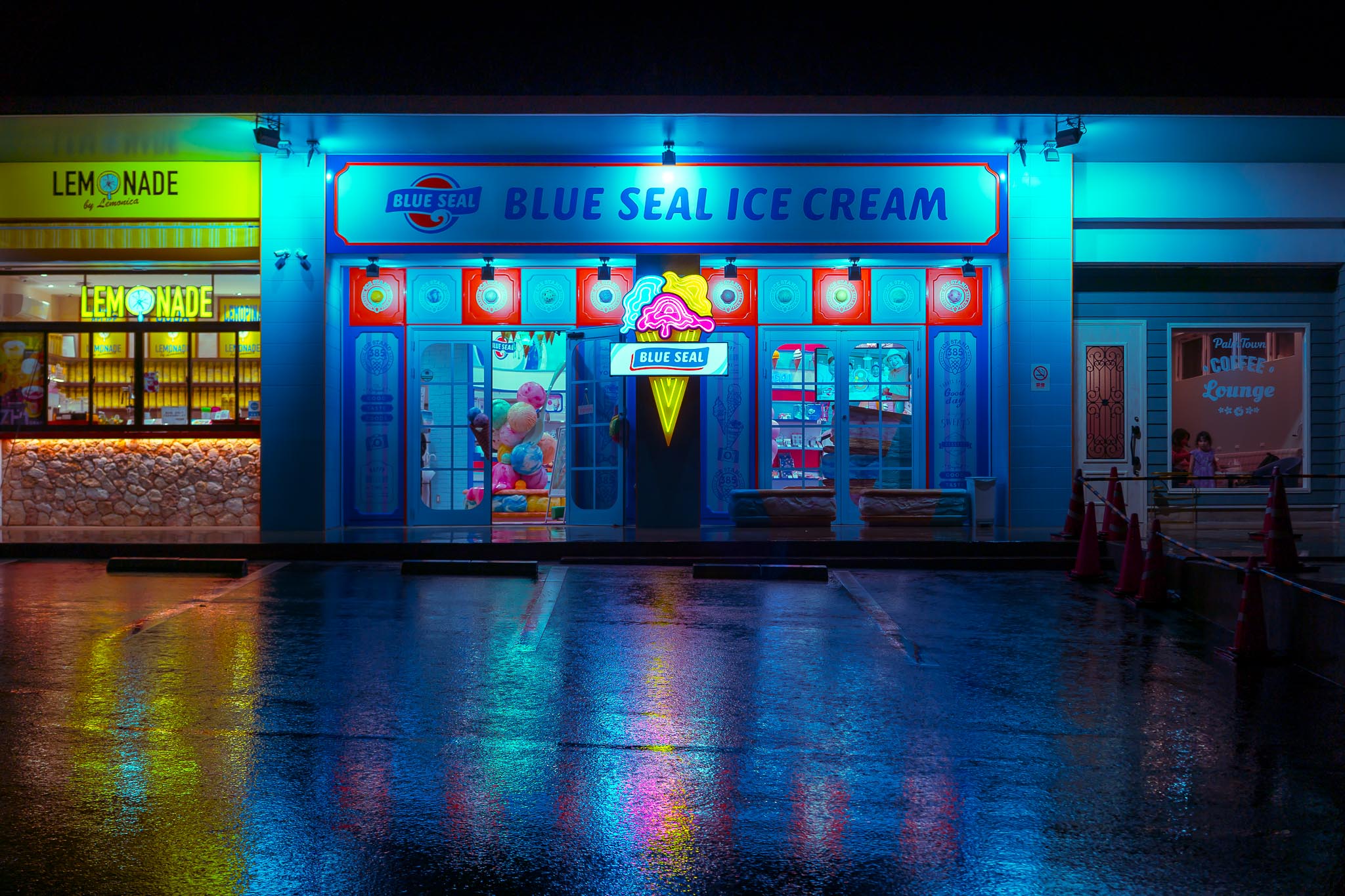 Blue Seal Ice Cream storefront at night in Okinawa — neon blue and yellow in the rain