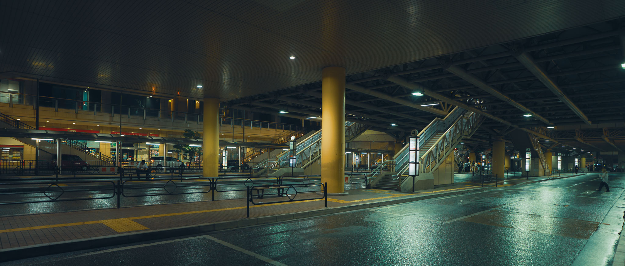 Wide, empty covered pedestrian deck outside Tachikawa Station at night with escalators and concrete pillars