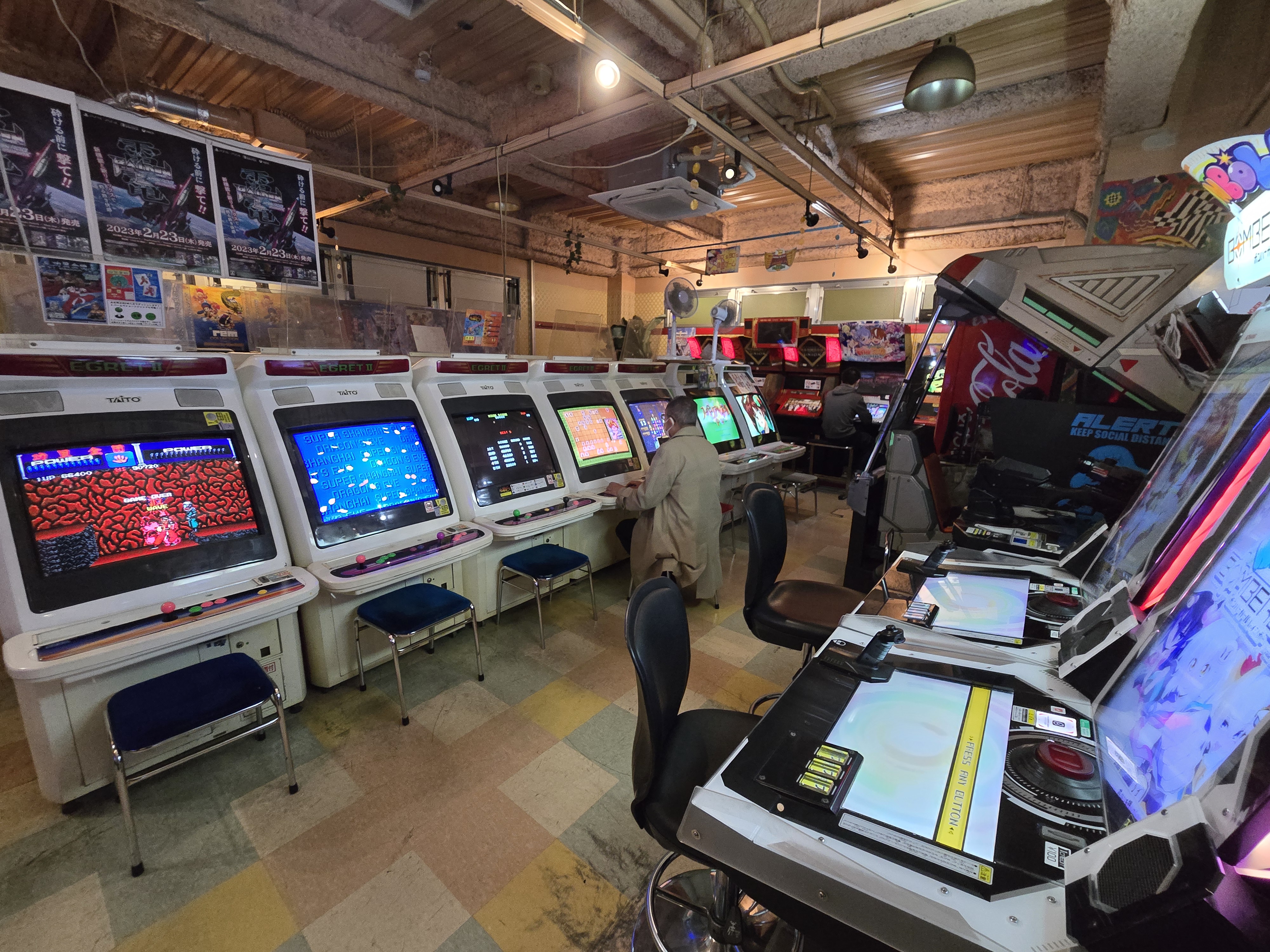 Game Center Mikado Takadanobaba — ambient floor shot, player at cabinet, exposed ceiling