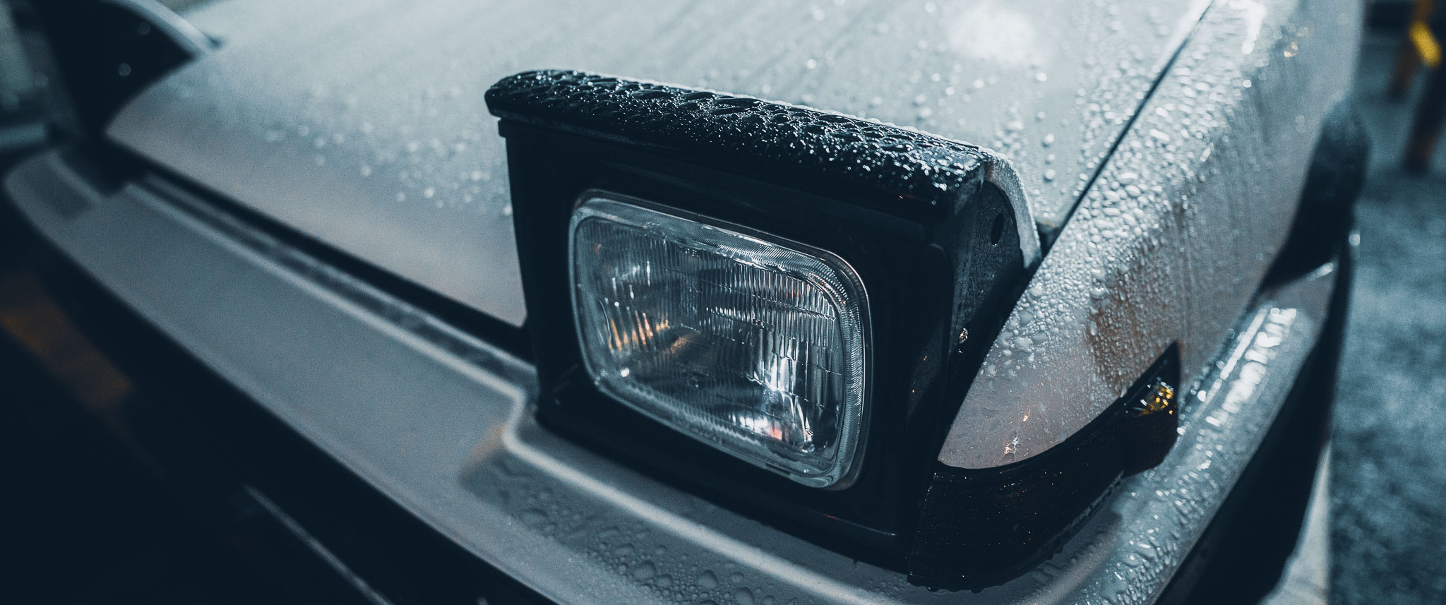 Toyota AE86 pop-up headlight close-up in the rain — wet bodywork detail