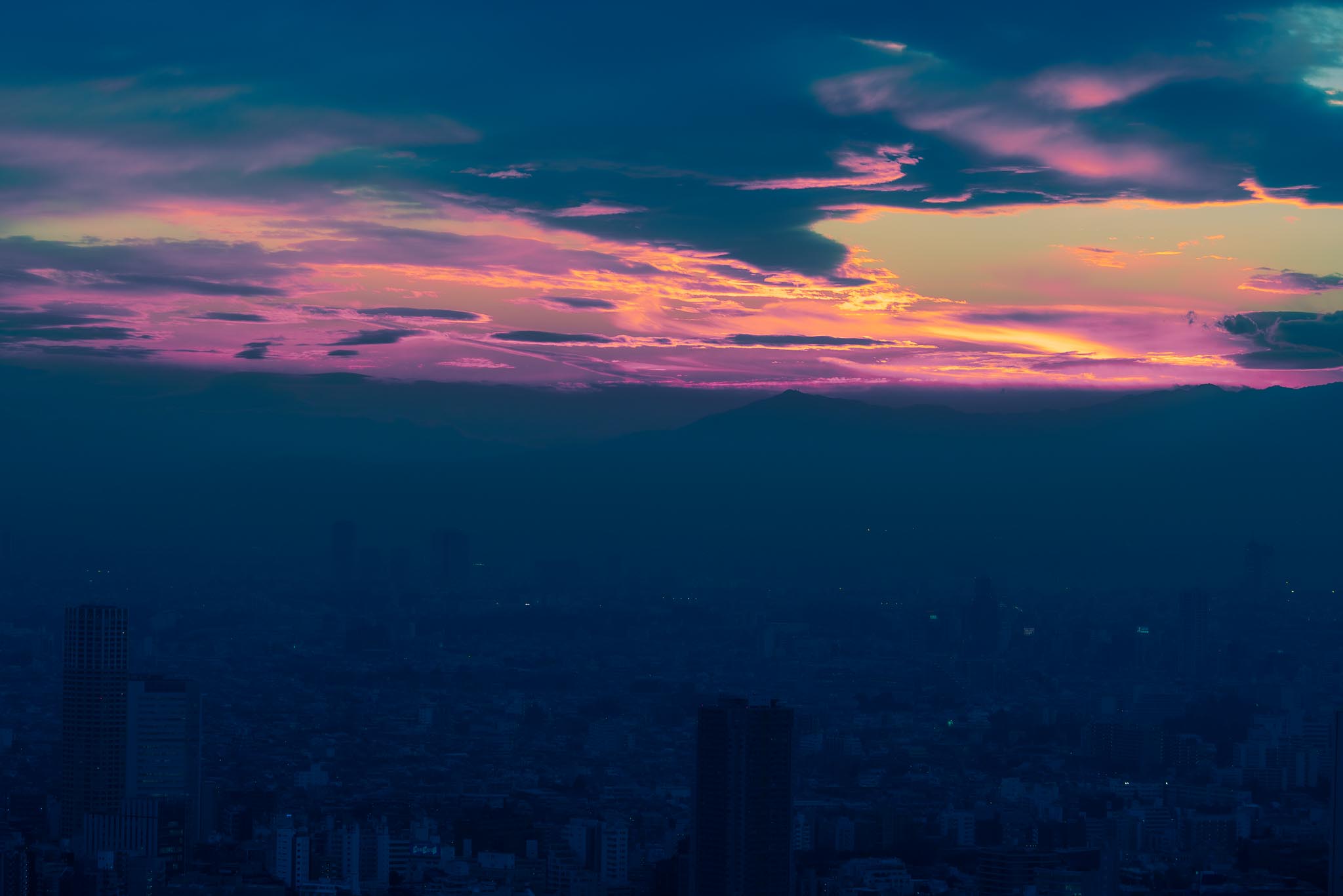 Dramatic sunset over Tokyo from Mori Tower — orange and pink clouds over mountains